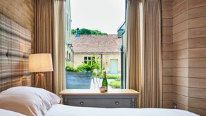 A hotel room with a bed, a bedside table with a bottle and glasses, and a window with curtains. - The Carriage House (Hexham)
