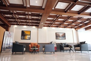 A reception area with a wooden ceiling, four sofas, a small table with a vase, and two framed pictures on the wall.