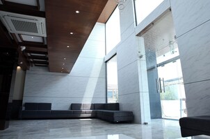 A modern lobby with a sectional sofa, marble flooring, and large windows allowing natural light.