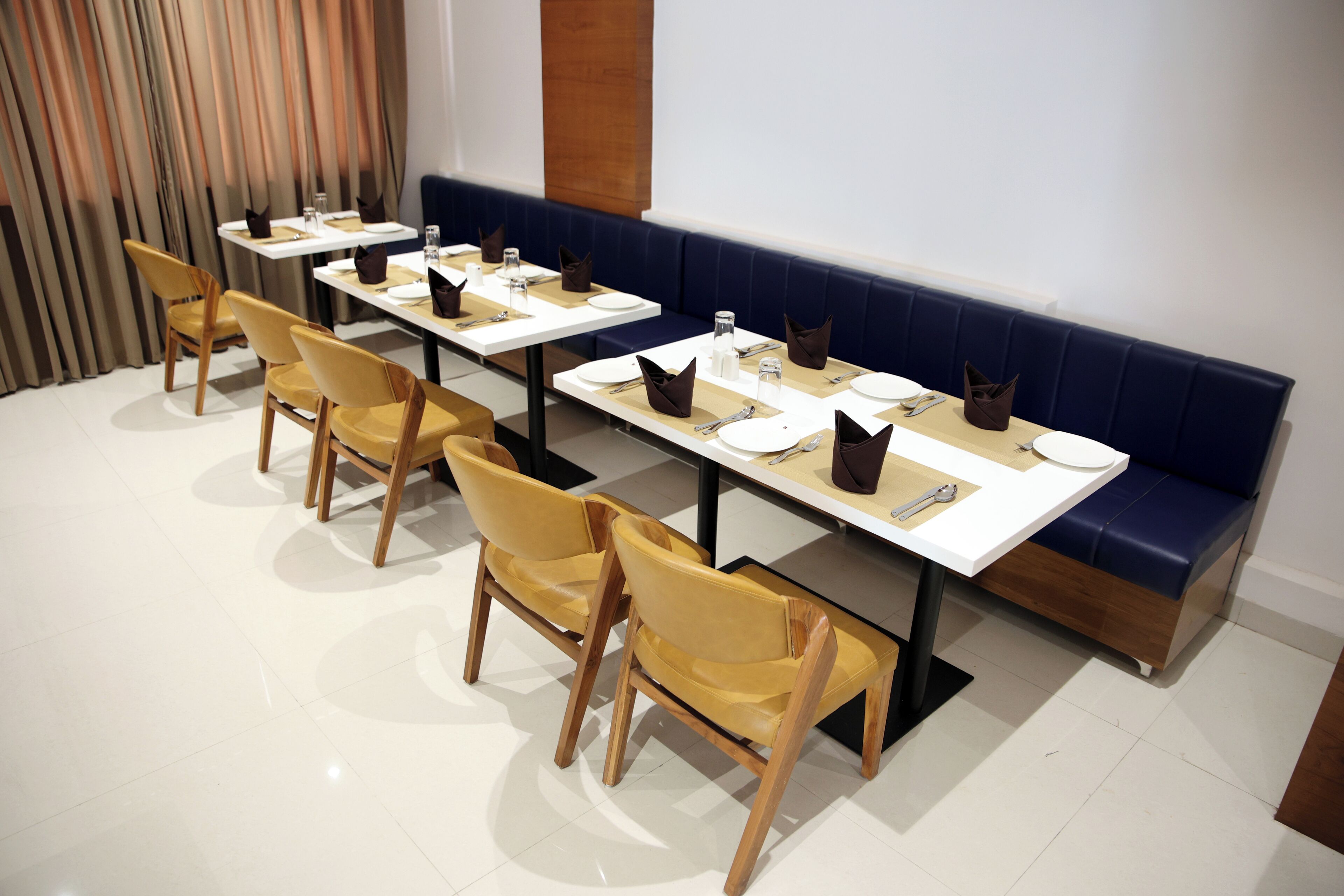 A dining area with multiple tables and chairs, a blue cushioned bench, and a modern interior design.