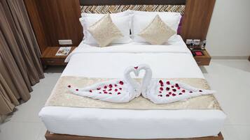 Una cama bien hecha con dos almohadas con forma de cisne, una mesita de noche de madera con un libro rojo y una botella de agua, y un cabecero estampado.
