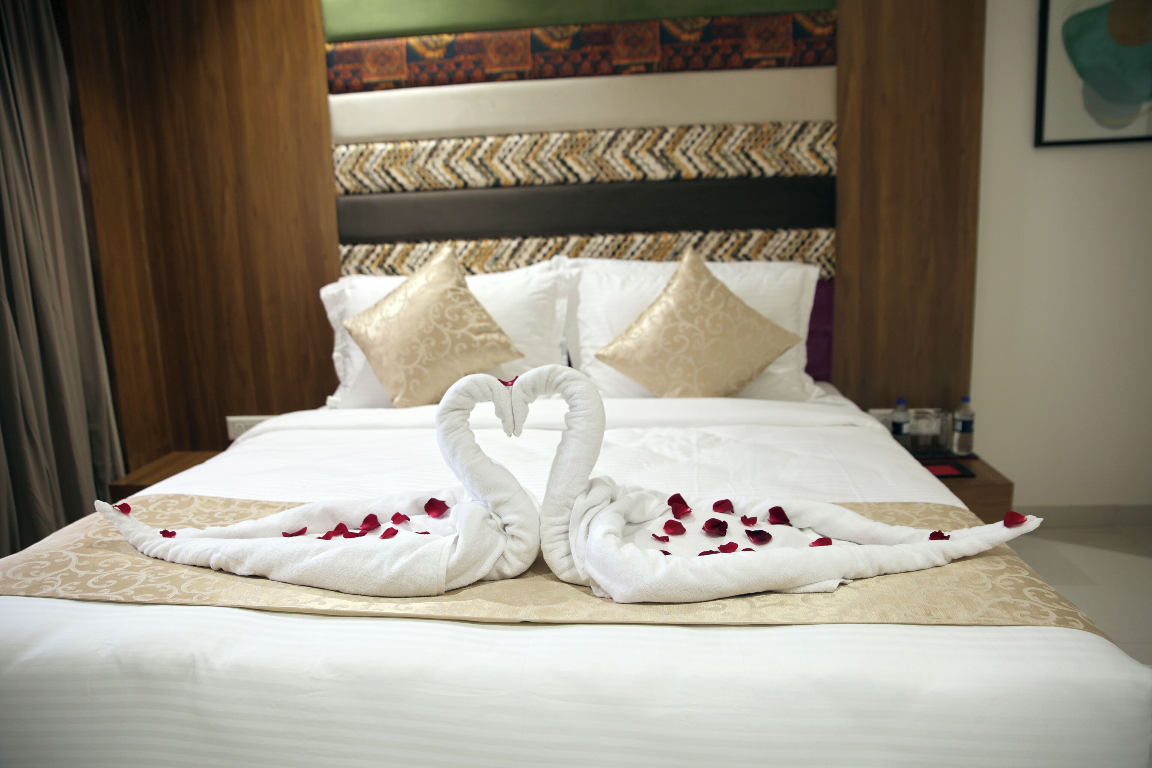 A bed with a decorative swan towel arrangement and rose petals.