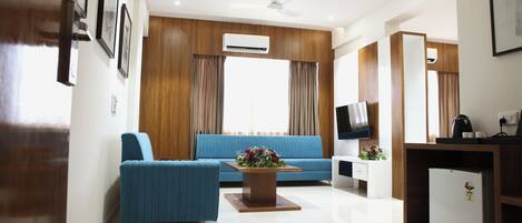 A modern living room with a blue sofa, a wooden coffee table, a flat-screen TV, and a mini-fridge.
