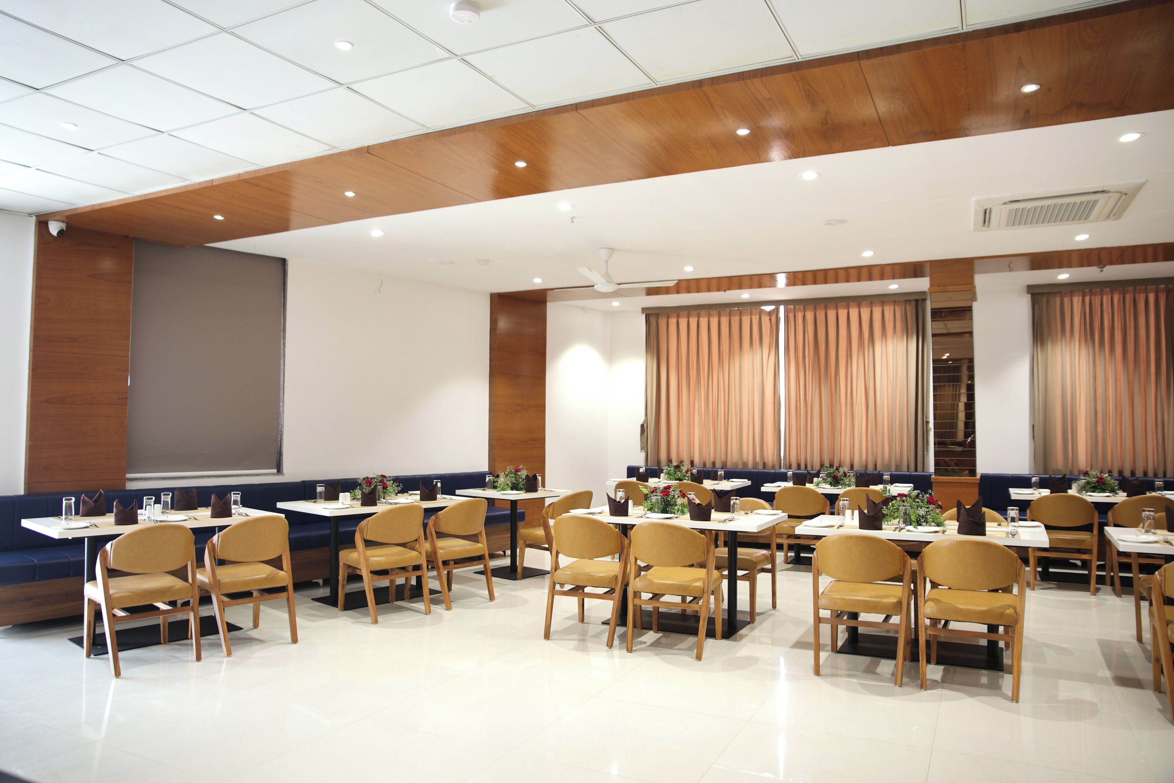 A conference room with multiple tables and chairs, a large screen, and a wooden ceiling.