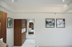 A modern hotel room with a wooden wardrobe, a bed with pillows, and two abstract paintings on the wall.