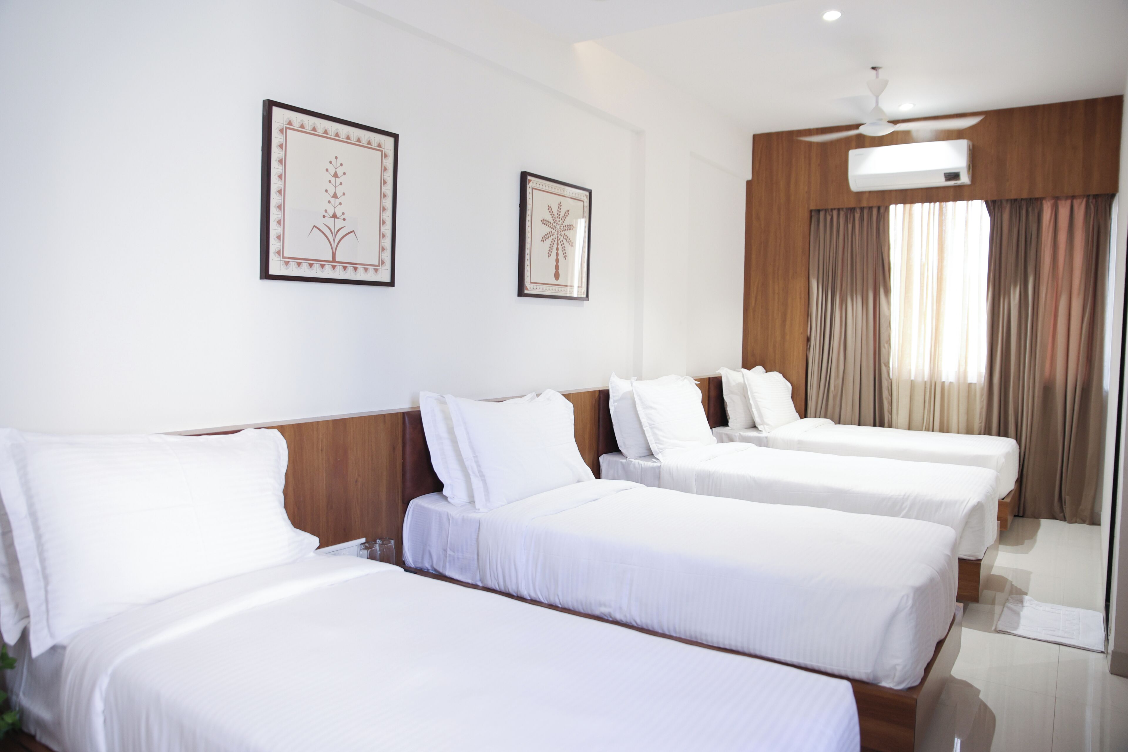 A hotel room with three single beds, a ceiling fan, and two framed wall art pieces.