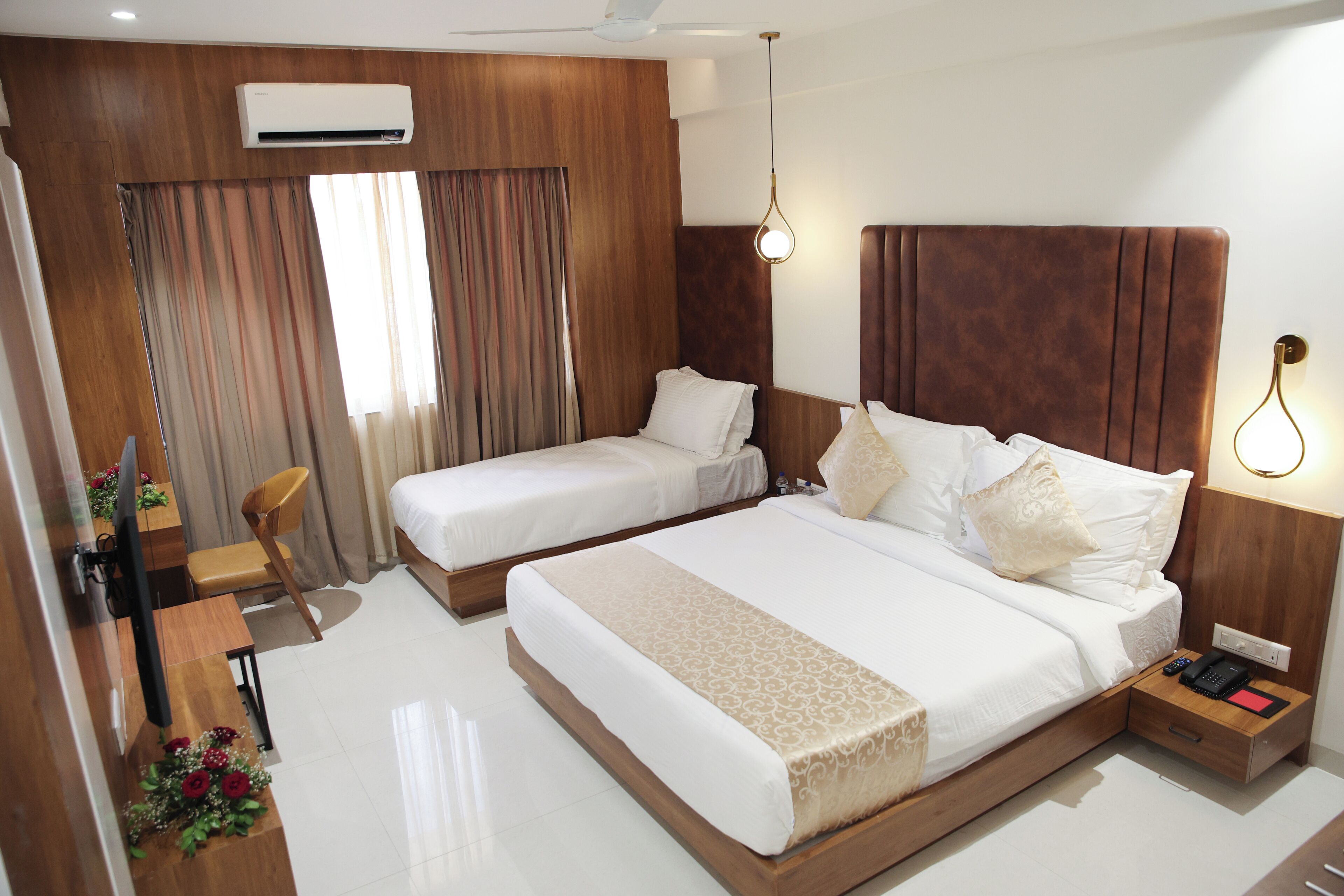Ein Hotelzimmer mit einem großen Bett, einem kleineren Bett, einem Schreibtisch mit Stuhl, einem Fernseher und einer Klimaanlage.