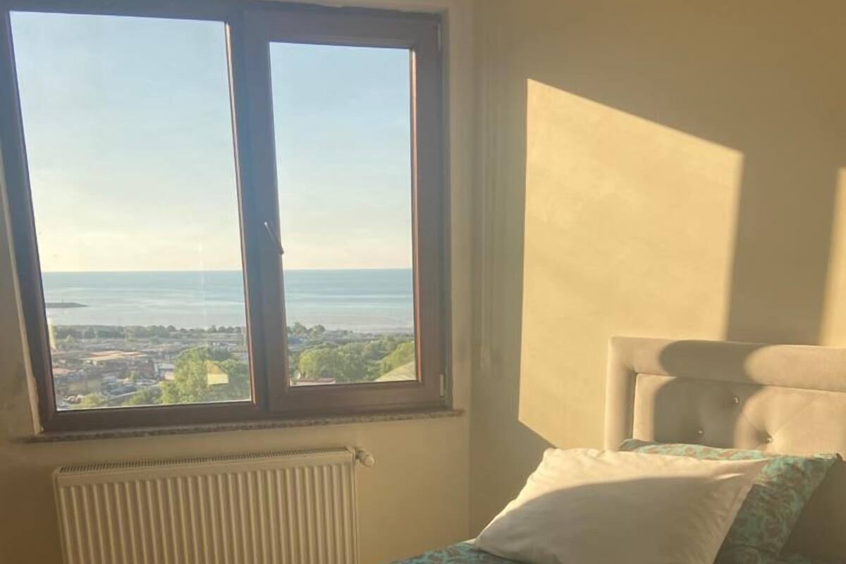 A bedroom with a large window, a bed with a patterned bedspread, and a radiator.