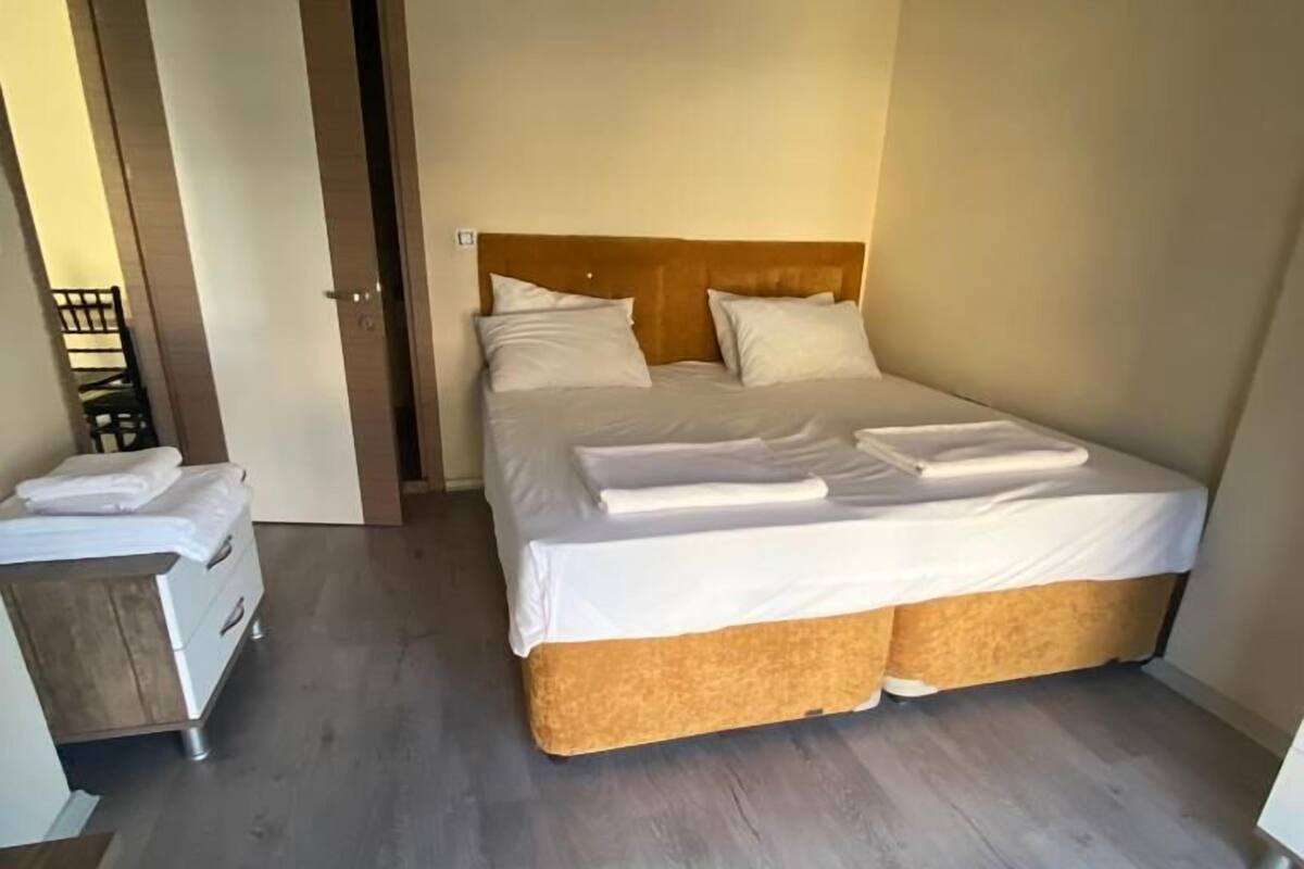 A bedroom with a bed, bedside table, and a door leading to another room.