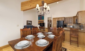 Un comedor con una mesa de madera dispuesta para seis personas, una araña y armarios de madera al fondo.