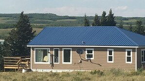 Une maison de plain-pied avec un toit bleu, entourée d’un champ verdoyant et d’arbres.