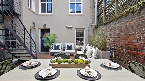A dining area with a table set for four, surrounded by wicker chairs, a brick wall, and a staircase.