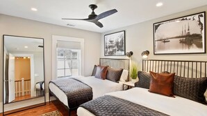 A bedroom with two beds, a ceiling fan, a large framed picture, and a mirror.