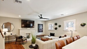 A modern living room with a fireplace, a dining area with leather chairs, and a large TV mounted on the wall.