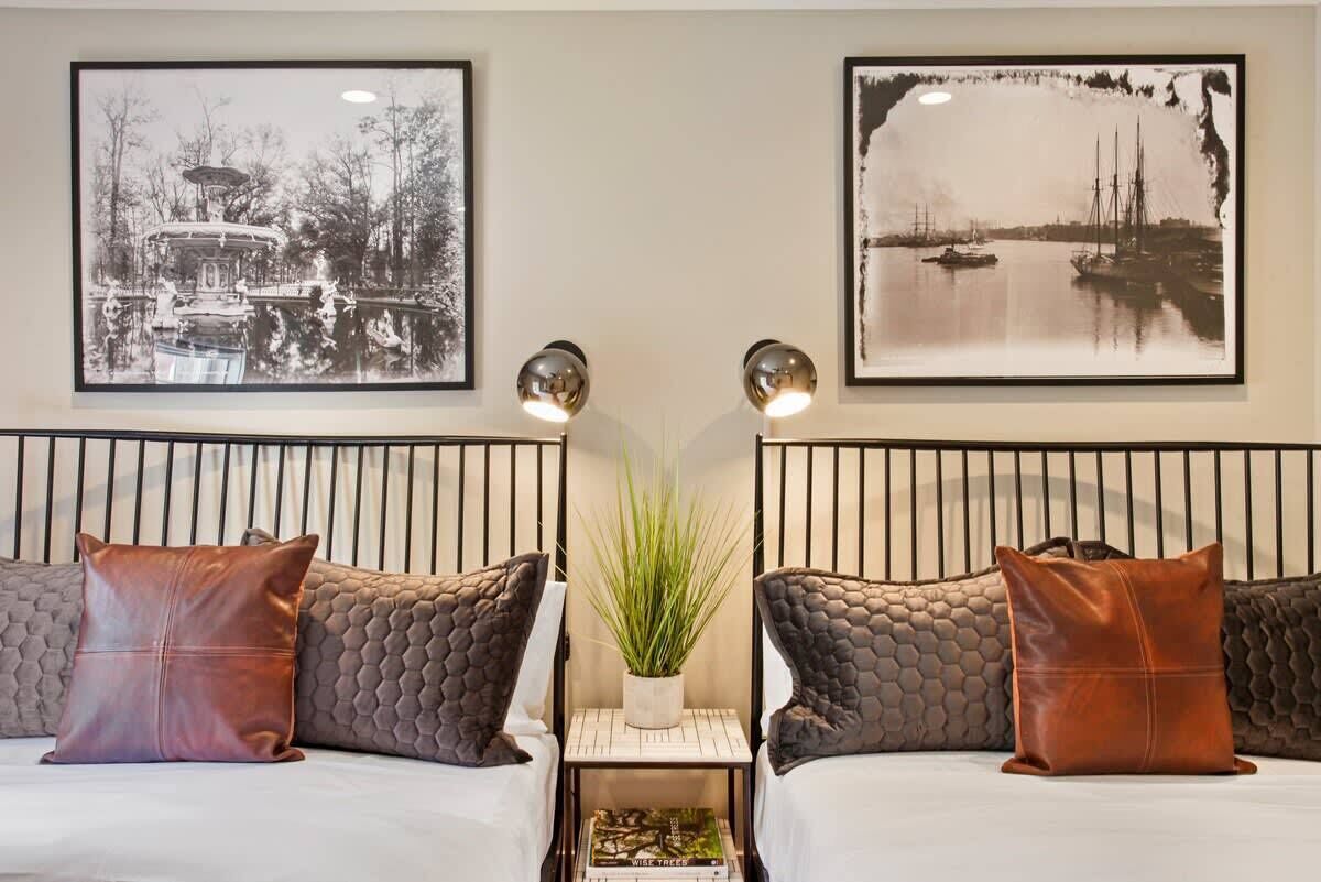 Une chambre d’hôtel avec deux lits, une table de chevet ornée d’une plante et deux tableaux encadrés accrochés au mur.