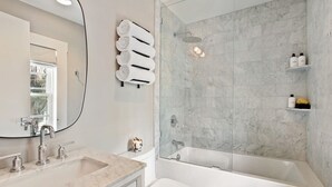 A modern bathroom with a marble sink, a toilet, a bathtub, and a glass-enclosed shower.