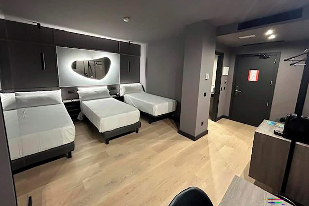 A hotel room with two single beds, a large mirror, and a kitchenette.