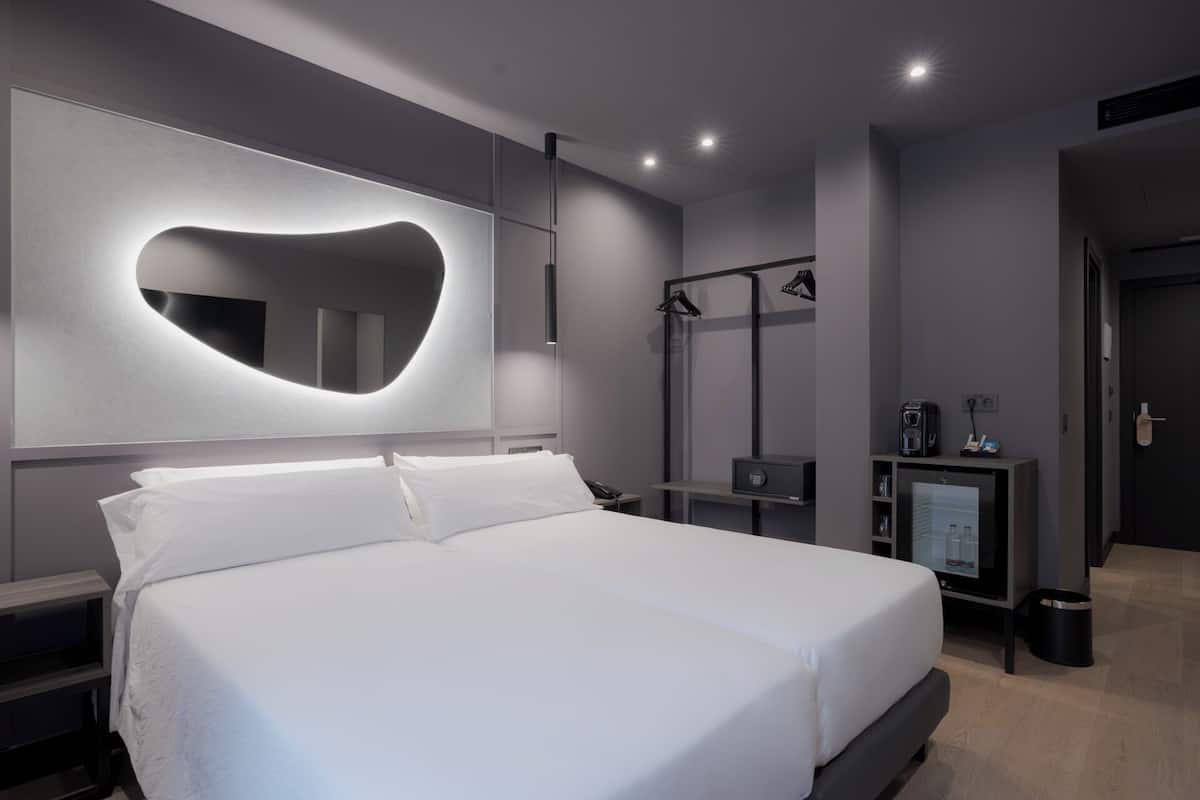 A modern bedroom with a large bed, a heart-shaped mirror, a TV, and a small desk with a coffee machine.