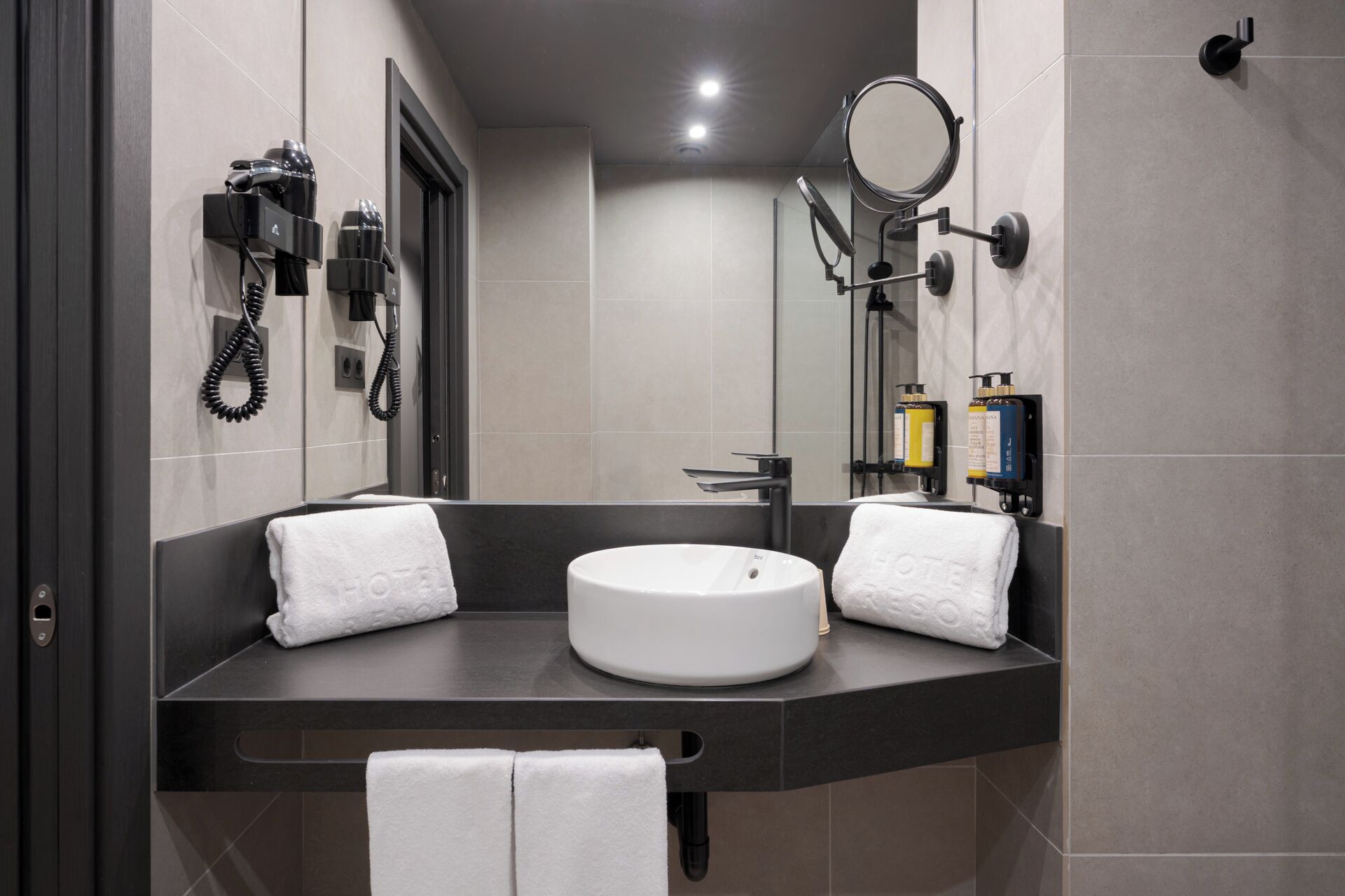 A modern bathroom with a round sink, two towels, a hairdryer, a mirror, and toiletries.