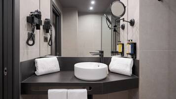 A modern bathroom with a round sink, two towels, a hairdryer, a mirror, and toiletries.