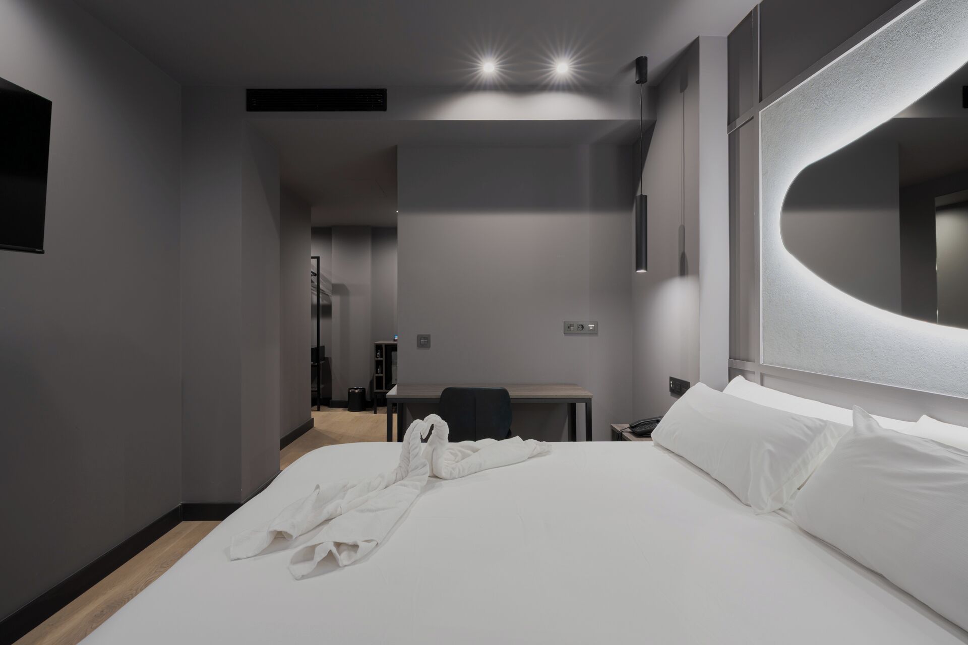 A modern hotel room with a large bed, a desk, and a mirror.