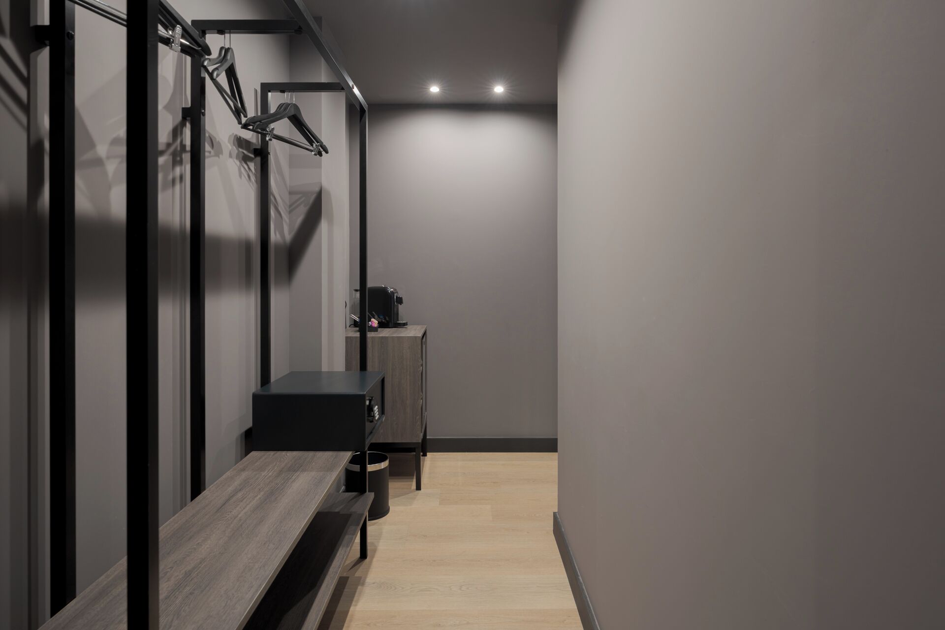 Un couloir moderne avec un banc, une machine à café et un porte-objets fixé au mur.