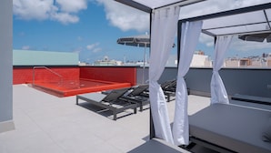 A rooftop terrace with a red pool, lounge chairs, and a view of the city skyline. - Hotel LIVVO La Escarlata (Las Palmas de Gran Canaria)