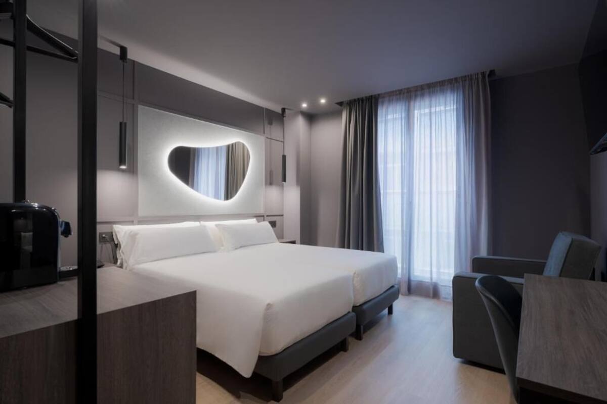 A modern hotel room with a large bed, a desk, and a chair.