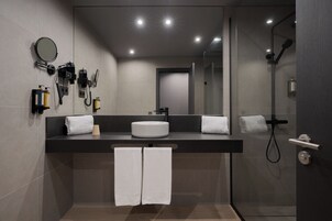 A modern bathroom with a round mirror, a white sink, and a glass-enclosed shower.