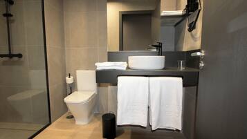 Ein modernes Badezimmer mit Duschkabine aus Glas, einer weißen Toilette, einem großzügigen weißen Waschbecken und einem Handtuchhalter mit zwei Handtüchern.