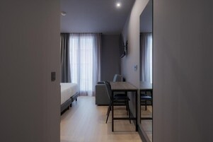 Una habitación de hotel moderna con una cama, un escritorio y una silla, un ventanal con cortinas y un televisor montado en la pared.