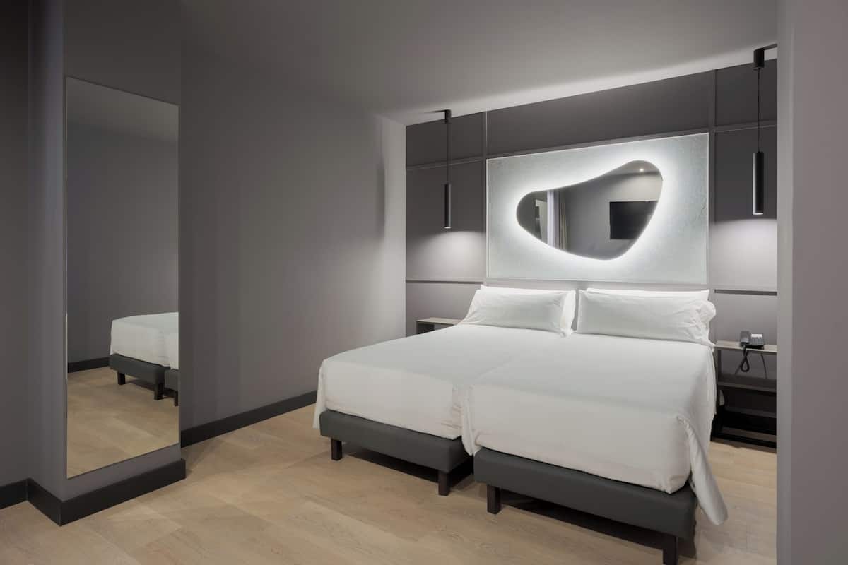 A modern bedroom with a large bed, a heart-shaped mirror, and a bedside table with a phone.