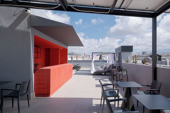 Terraço no telhado com parede vermelha, assentos ao ar livre e vista para a paisagem urbana.
