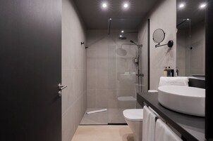A modern bathroom with a glass-enclosed shower, a round mirror, and a white sink with a towel.