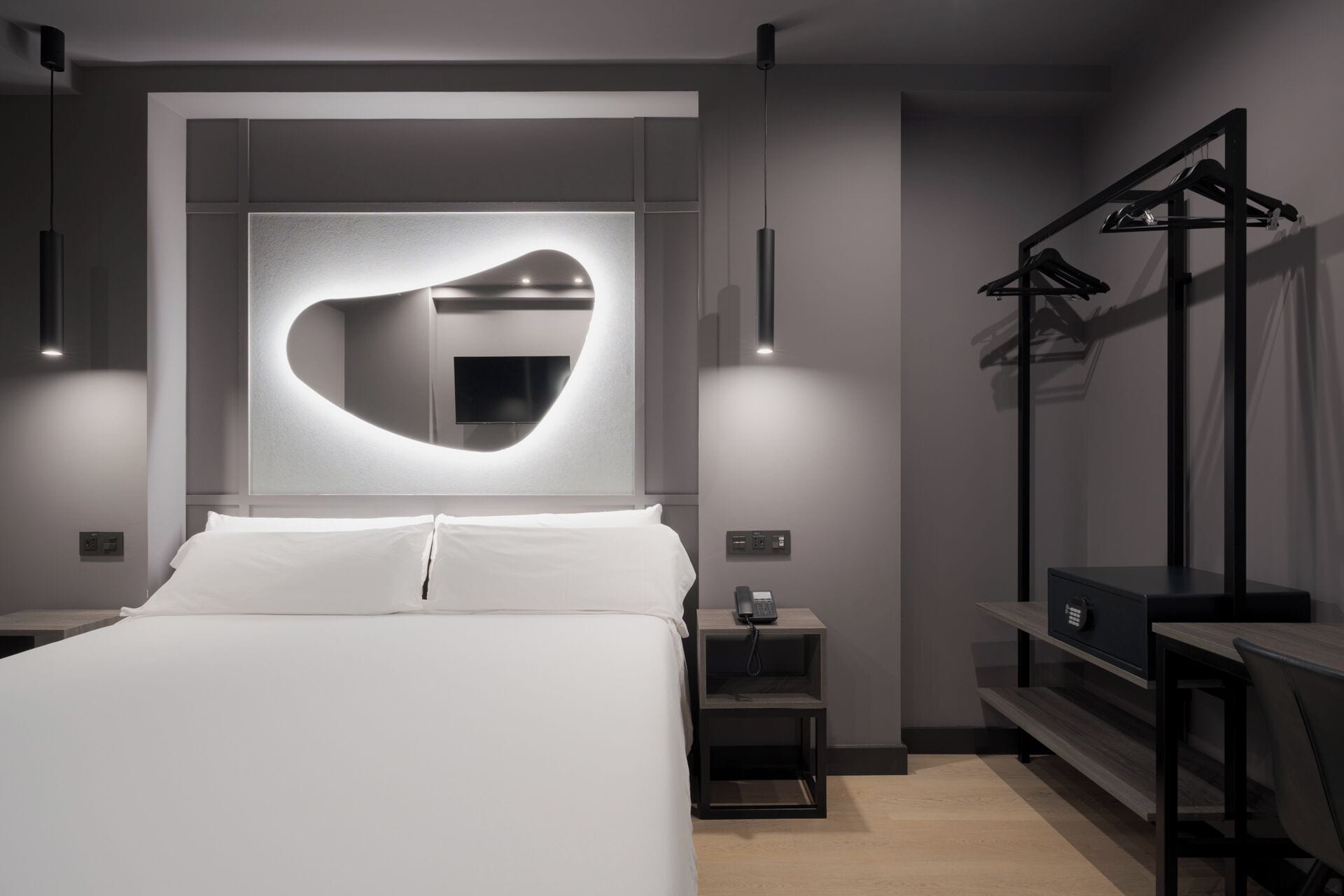 Una habitación de hotel moderna con una cama grande, un espejo integrado, mesitas de noche y un armario con espacio para colgar.