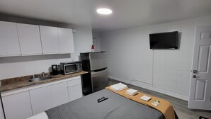 A compact kitchen with white cabinets, a microwave, a refrigerator, and a sink. - Happyland Inn (Severn)