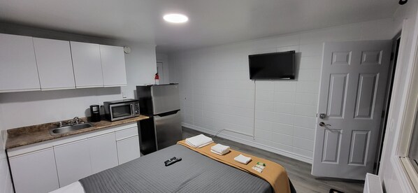 A compact kitchen with white cabinets, a microwave, a refrigerator, and a sink. - Happyland Inn (Severn)