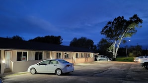 A motel with a single-story structure, a parking lot, and a tree in the background. - Happyland Inn (Severn)
