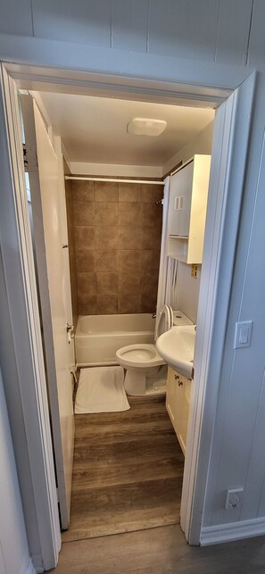 Un baño con bañera, inodoro y lavamanos, con suelo de madera y azulejos color beige.