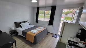 A hotel room with a bed, a desk, a chair, a window with curtains, a radiator, and a view of the outside. - Happyland Inn (Severn)