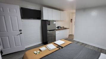Una cocina compacta con armarios blancos, un refrigerador de acero inoxidable y un microondas. En primer plano, una pequeña mesa con una manta y toallas.