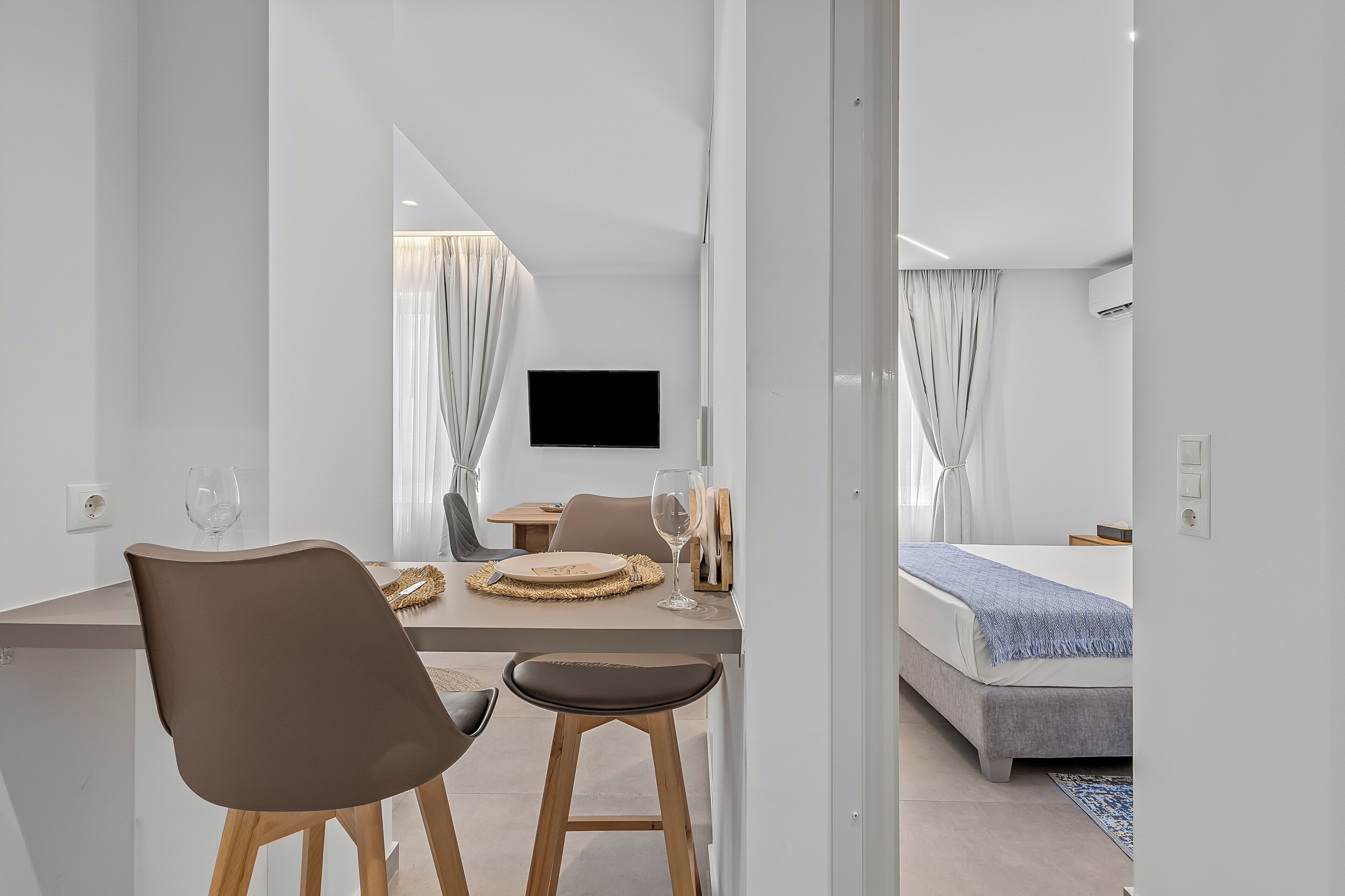 A modern hotel room with a dining area, a bed, and a TV mounted on the wall.