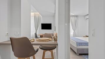 A modern hotel room with a dining area, a bed, and a TV mounted on the wall.