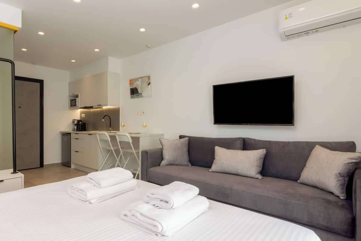 A modern hotel room with a large bed, a grey sofa, and a flat-screen TV.