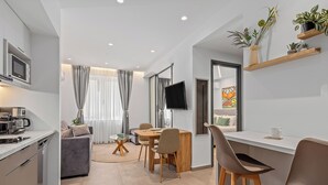 A modern kitchen with a built-in microwave, a dining area with a round table and chairs, a sofa, and a TV mounted on the wall. - Athens Theatrou Apartments (Athens)