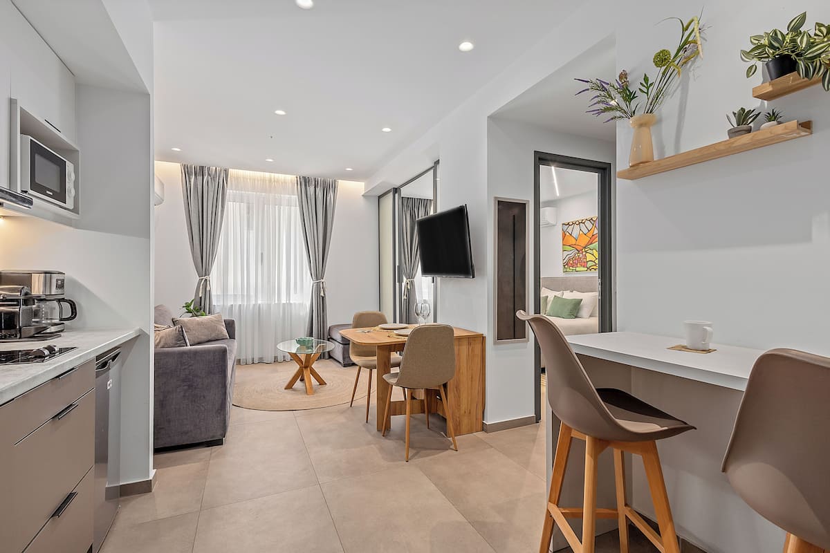 A modern kitchen with a built-in microwave, a dining area with a round table and chairs, a sofa, and a TV mounted on the wall.
