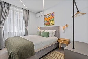 A bedroom with a bed, bedside tables, a hanging light, a wall-mounted air conditioner, and a painting. - Athens Theatrou Apartments (Athens)