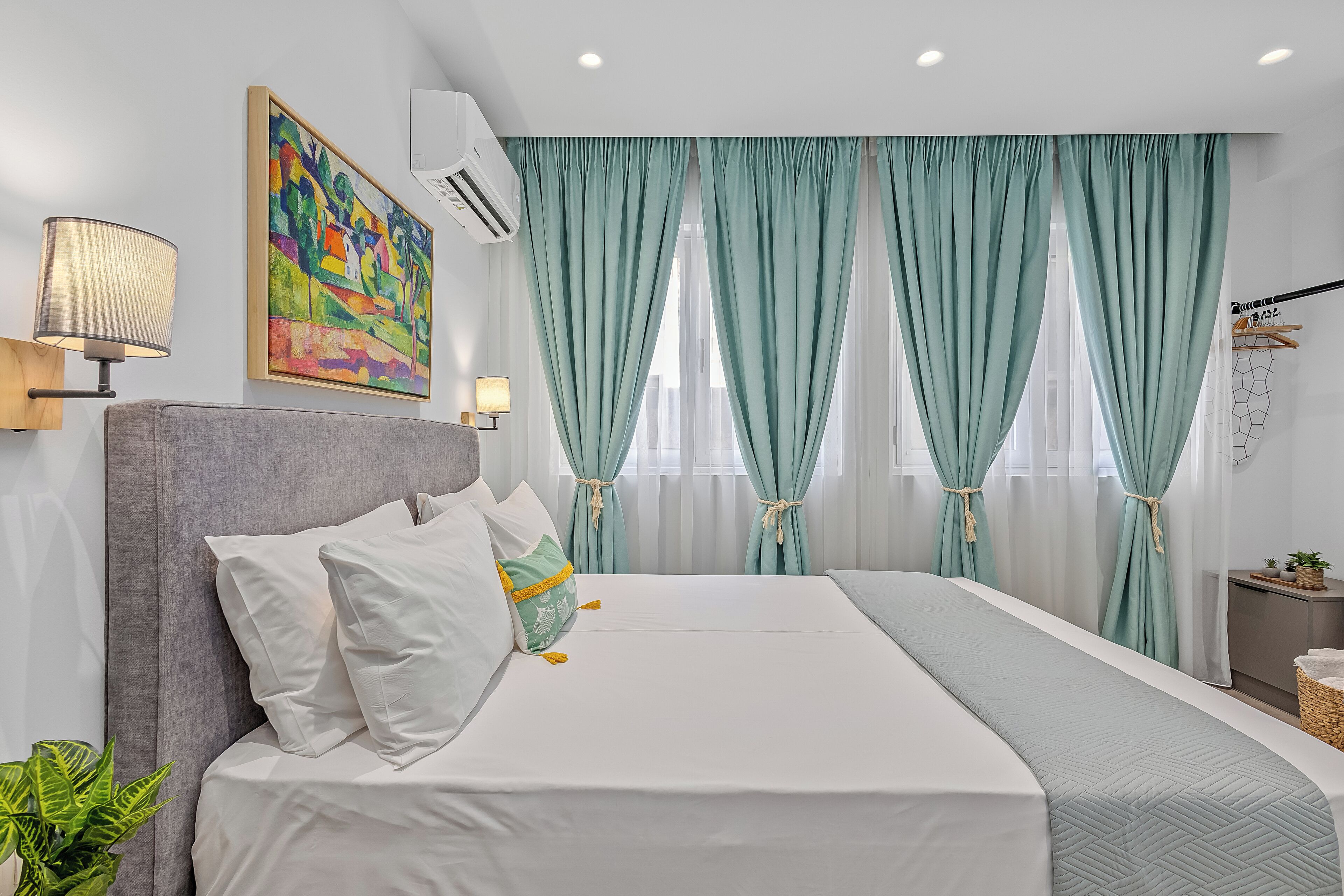 A modern bedroom with a large bed, a painting, an air conditioning unit, and a window with curtains.