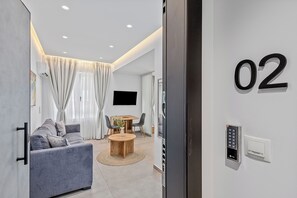 A modern living room with a sofa, a dining table, and a TV. - Athens Theatrou Apartments (Athens)
