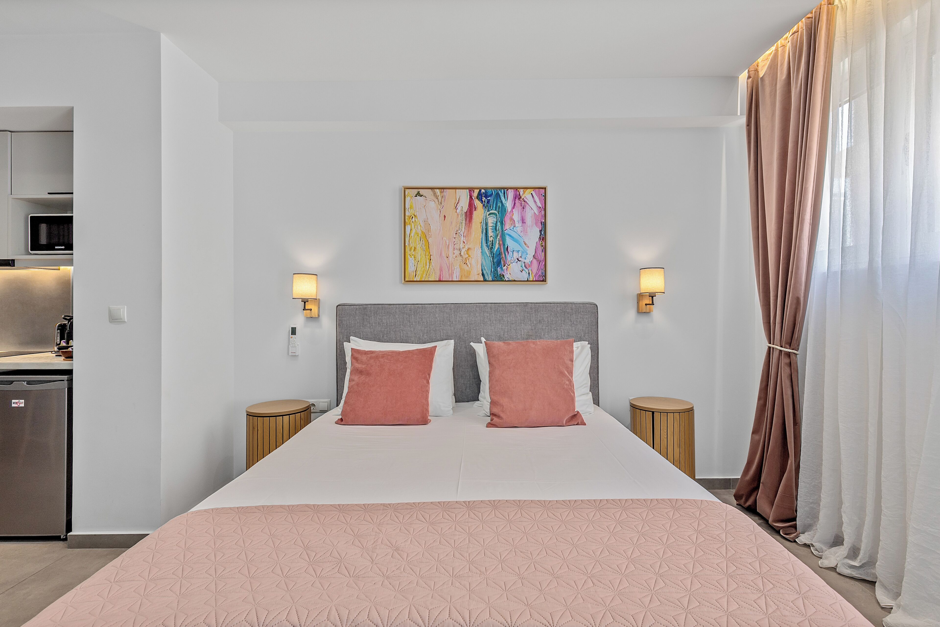 Quarto de hotel com cama, duas luminárias de cabeceira, um quadro na parede e vista para o exterior.